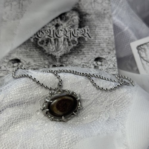 Wyjątkowy, ręcznie stworzony wisiorek z eye agate, agatem o umaszczeniu w kształcie oka, który stanowi centralny punkt naszyjnika. Wyjątkowy wygląd podkreślony jest ręcznie wykonaną oprawą inspirowaną starymi, ornamentalnymi wisiorkami dam dworu.