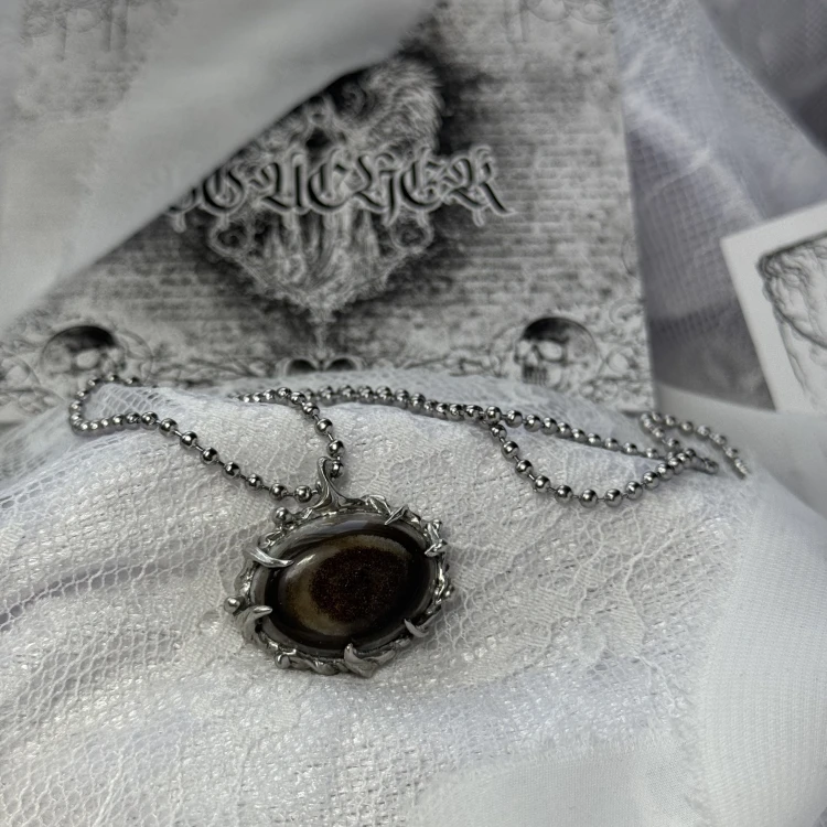 Wyjątkowy, ręcznie stworzony wisiorek z eye agate, agatem o umaszczeniu w kształcie oka, który stanowi centralny punkt naszyjnika. Wyjątkowy wygląd podkreślony jest ręcznie wykonaną oprawą inspirowaną starymi, ornamentalnymi wisiorkami dam dworu.